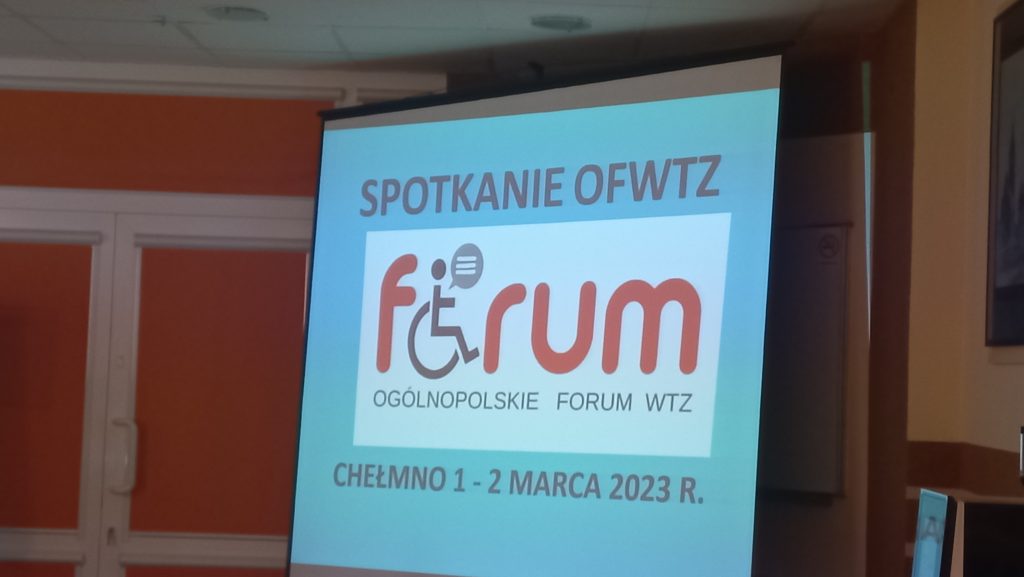 Na ekranie z projektora wyświetlony slajd koloru niebieskiego z czerwonym logiem forum ogólnopolskiego forum wtz. Spotkanie 1-3 marzec Chełmno